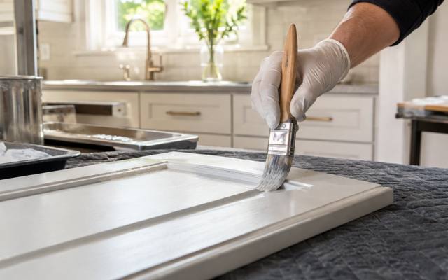 A brush cutting white paint along the edge of a cabinet door.